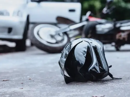 Close-up of a black biker helmet on the street with overturned motorbike in the background. Road collision concept